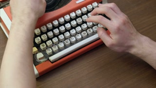 Man's hands typing on an old red mechanical typewriter
