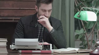 Focused man reading book at desk with typewriter