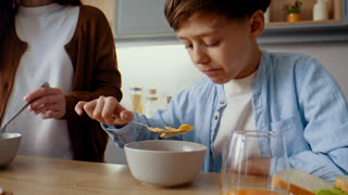 boy eats corn flakes with milk and nods head to mother