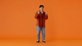 Asian guy clapping and showing thumbs up in orange studio