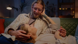 Woman lying on husband knees while relaxing on couch indoors