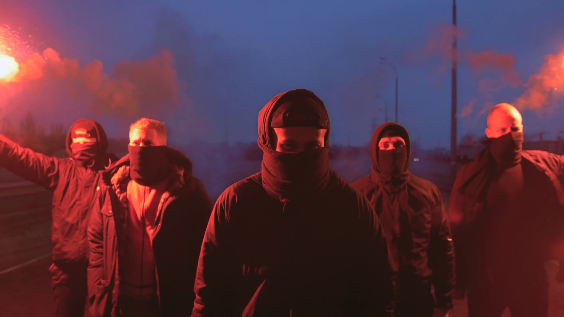 Group of young men in balaclavas with red burning signal flare walking