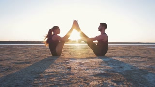 Two persons doing couple yoga nauka asana boat pose on the beach at sunset