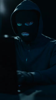 Hacker in and balaclava at laptop in dark room