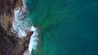 Top view of the ocean surface near the rocky coast off the island of Tenenife, Canary Islands, Spain. Aerial drone footage of sea waves reaching shore