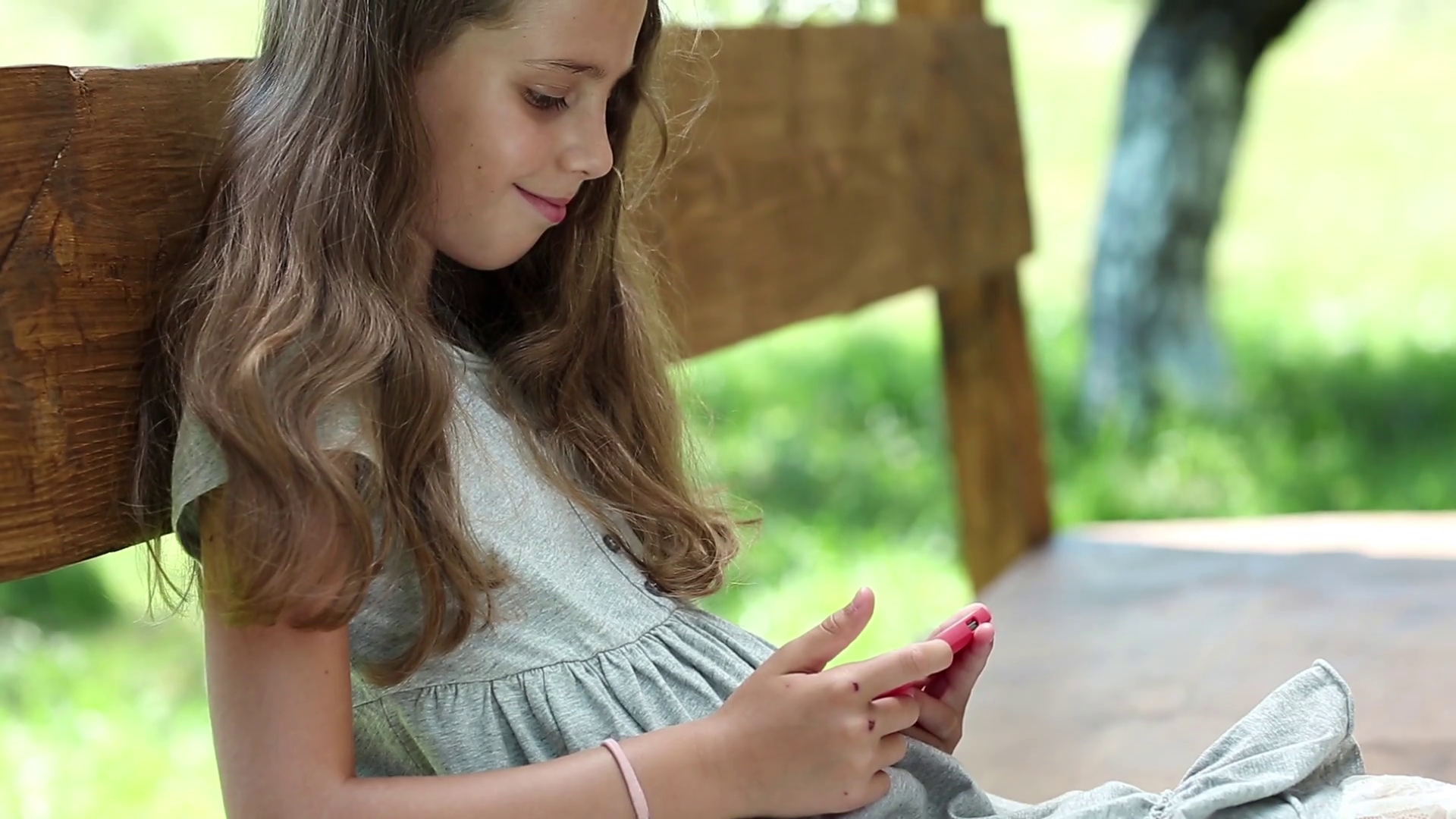 Beautiful girl with red smartphone sits on the bench. 
