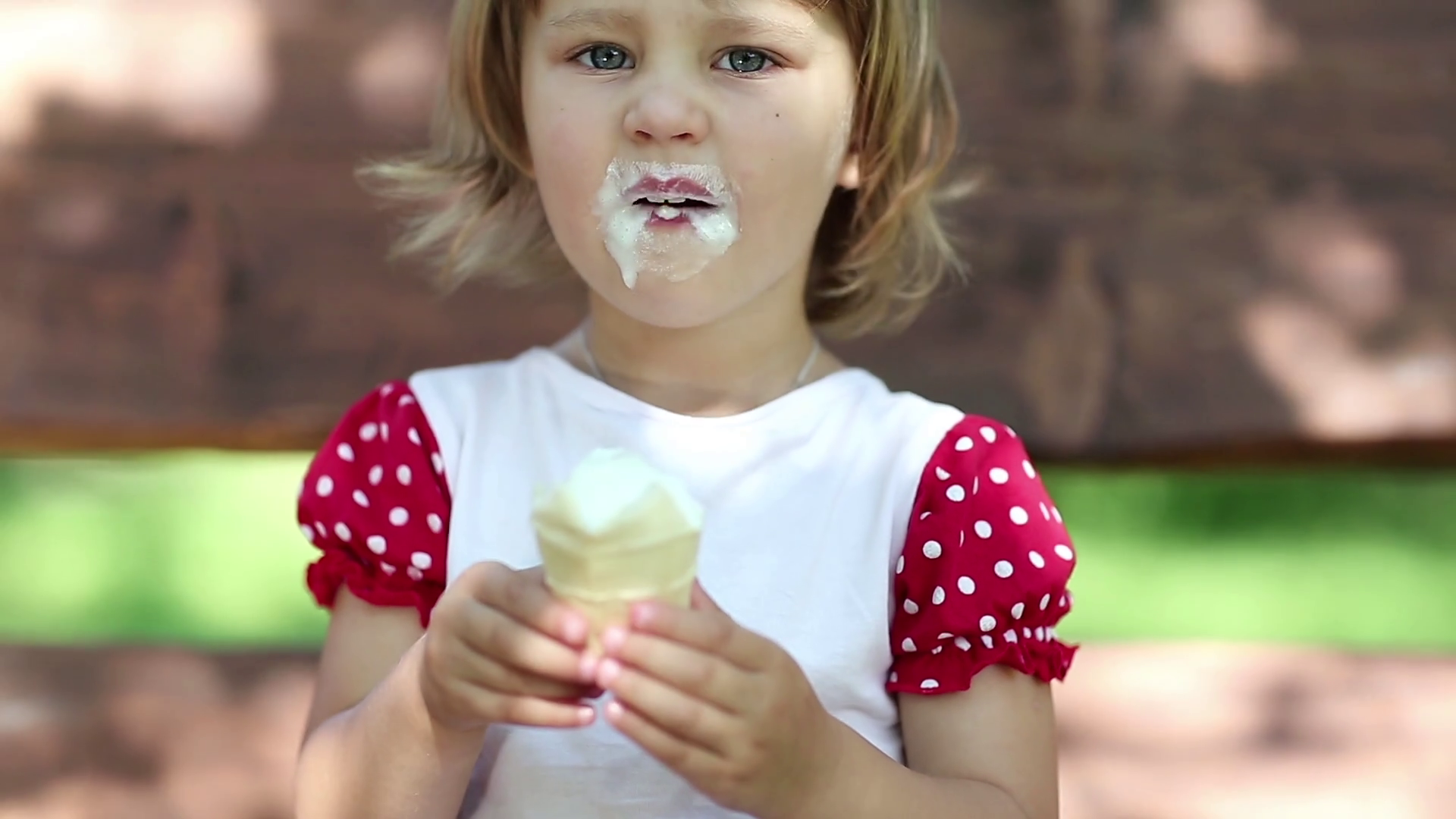 Little cheery girl sits on the swing bench eats ice cream and licks her