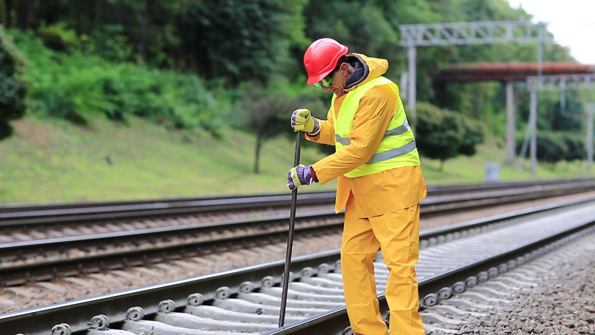 Railway worker in yellow uniform with crowbar in hands mends railway