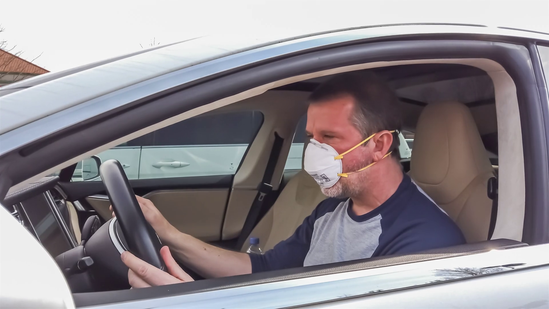 Mature male sitting behind the wheel in his car, wearing a face mask