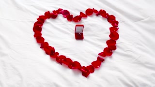 valentines day, proposal and romantic date concept - bed decorated with heart made of red petals and diamond engagement ring in gift box