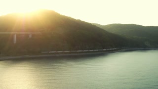 A train is going next to the green hills and the sea
