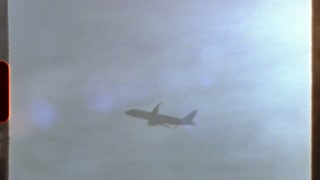 Filmed on super 8 film - airplane flying in a cloudy sky, with a retro 8mm or super 8 film effect and light leaks, creating a nostalgic and