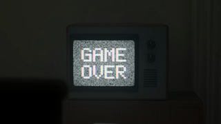 A 3D render of a retro television set in a dark room displaying a pixelated game over message on a static screen with white noise
