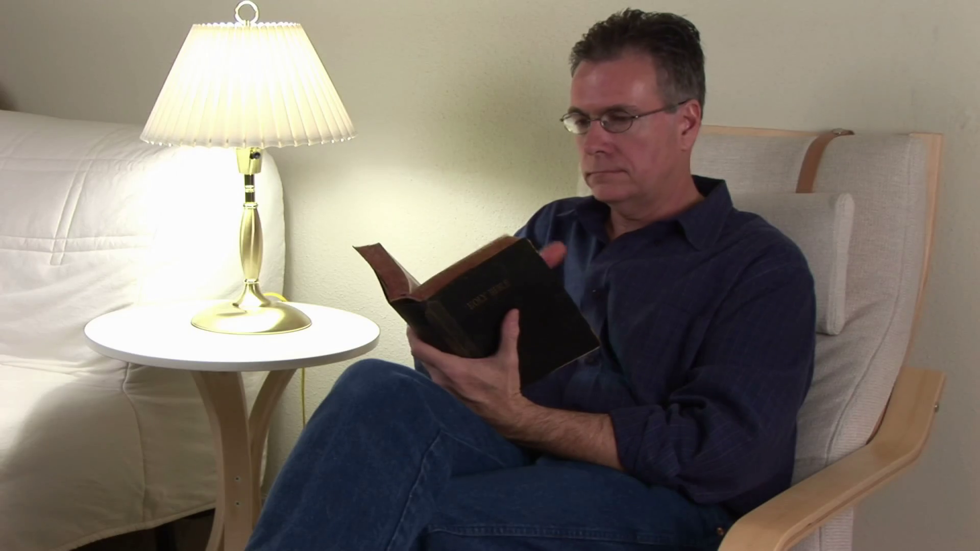 A man sitting in his reading chair studying his Bible stops and offers