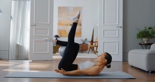 Woman practicing fitness routine at home on yoga mat in bright, modern living with natural light