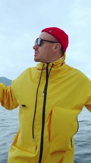 A Stylish Individual in a Yellow Rain Jacket and Red Beanie Enjoying a Scenic View on a Lake, Capturing a Moment of Joy and Freedom