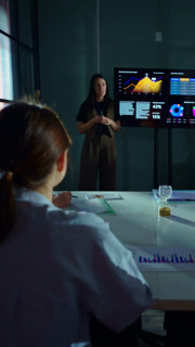 Businesswoman presenting financial analytics on digital screen during corporate meeting, explaining data charts and performance metrics to
