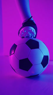 Close-up shots of a football player cleated foot resting on a classic black and white soccer ball under vibrant purple and blue studio
