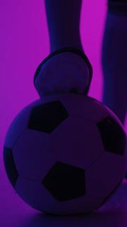 Close-up shots of a football player controlling a classic black and white soccer ball with cleats in a moody purple and blue lighting