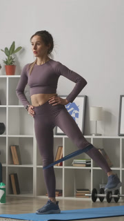 A woman performs resistance band exercises in her living room, focusing on fitness and strength training at home with workout gear on a mat