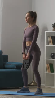 A fit woman in athletic wear performs a home workout in her living room, lifting a weight plate while standing on a yoga mat to strengthen