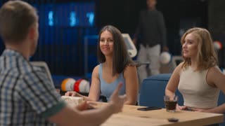 A joyful black African man runs up to friends giving five men and women sitting at a table in a bowling club. Celebrate victory and streak. To cut and congratulate on the victory. Team success.