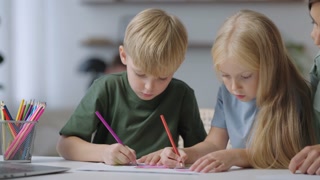 Two children draw together sitting at the table and mom helps. a boy and a girl draw together at a table