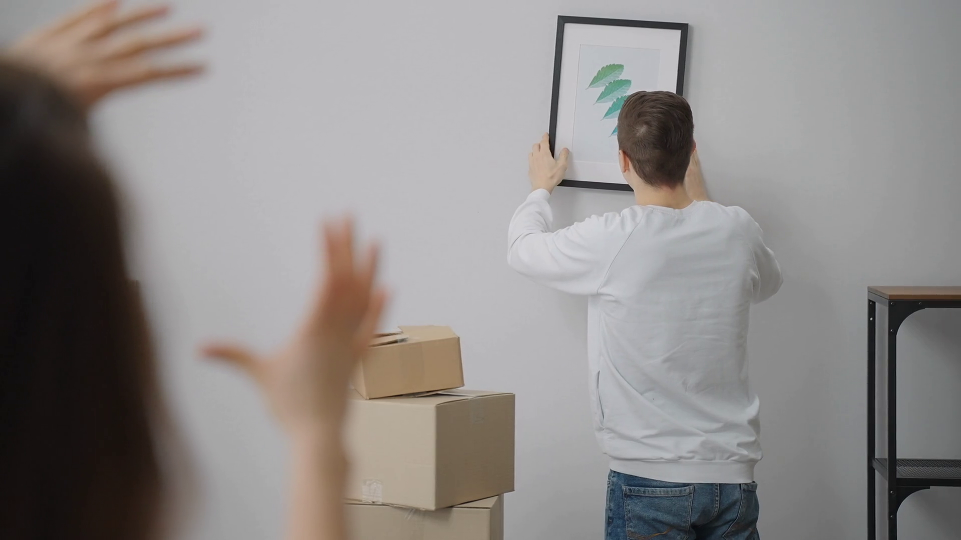 A man hangs a picture on the wall. The girl looks at the horizon and