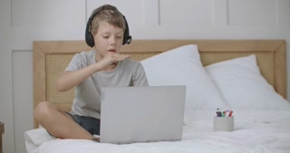 Child Engages in Online Conversation with Parents from Summer Camp, Seated on Bed