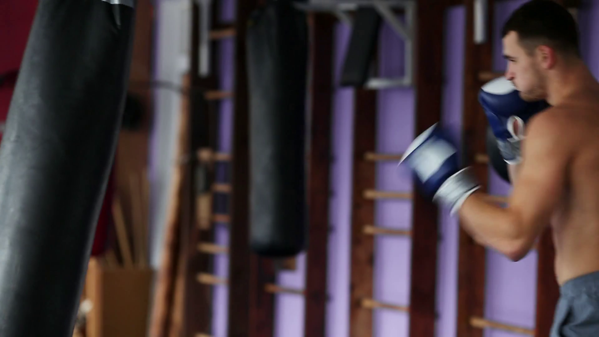 Muscular male professional boxer trains by punching bag at the gym in