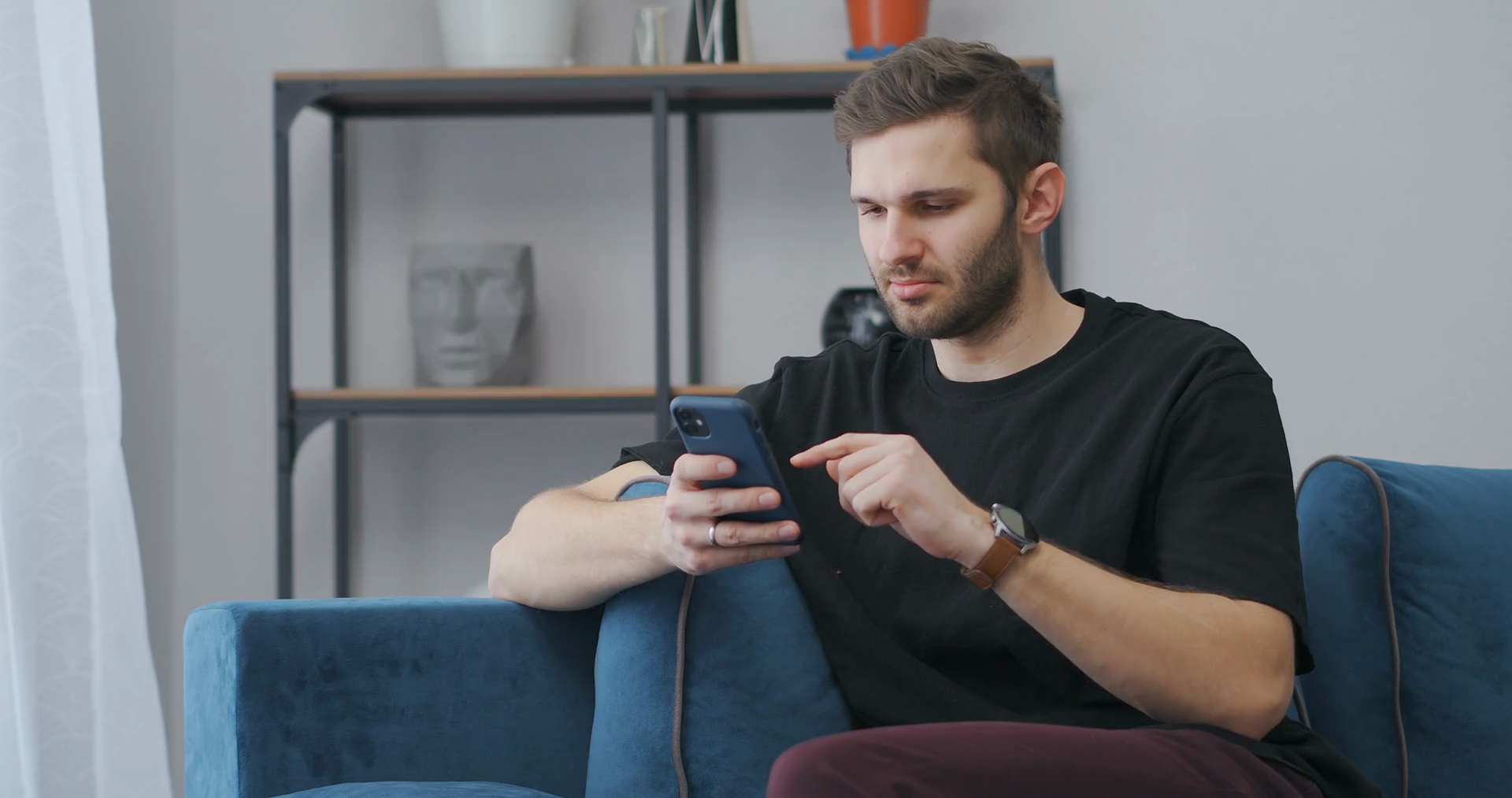 young man is using app in smartphone sitting at home, swiping screen of