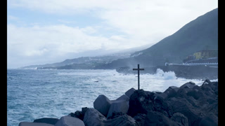 Rough ocean waves crashing on a rocky coastline with cross