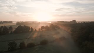 Golden sunrise illuminating misty fields and trees