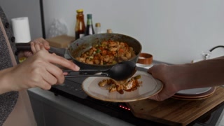 Close-up view of unknown girl putting teriyaki chicken on plate of unrecognisable man using plastic cooking spoon