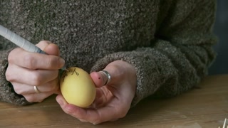 Close up of unrecognizable woman with black pen drawing branches with leaves on yellow Easter egg