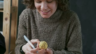 Medium shot of happy woman drawing ornament on colored Easter egg with black pen