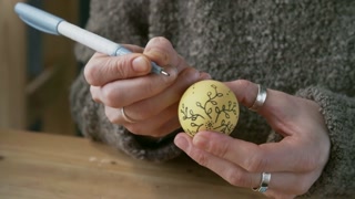 Close up of unrecognizable woman with black pen drawing beautiful ornament on colored Easter egg