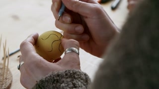 Over the shoulder shot of unrecognizable woman with black pen drawing ornament on colored Easter eggs