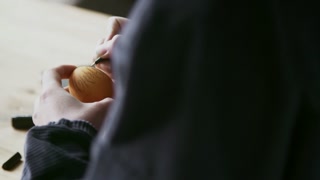Over the shoulder shot of unrecognizable woman with black pen outlining pattern on orange colored Easter egg