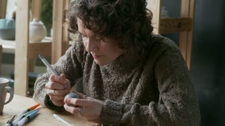 Medium shot of young woman with curly hair drawing hexagon pattern on Easter egg