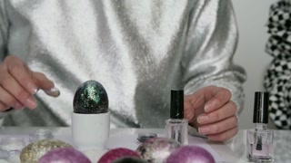 Mid-section shot of unrecognizable woman in shiny outfit decorating Easter egg with glitter