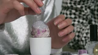Close up of unrecognizable woman sprinkling glitter on top of colored Easter egg in cup