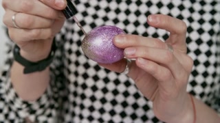 Mid-section shot of unrecognizable woman in stylish shirt with rhomb pattern painting Easter egg with nail polish and putting glitter on it