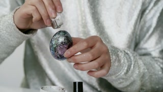 Mid-section shot of unrecognizable woman in shiny outfit decorating Easter egg with glitter and nail polish