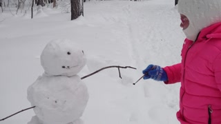 Child builds snowman in winter forest