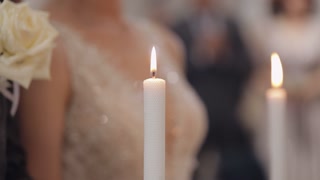 Close up view of bride and groom standing together and holding candles in hands during wedding ceremony in church