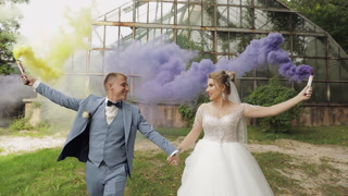 Happy Caucasian Newlywed couple kissing and Celebrating with Smoke bombs on their wedding day in park.