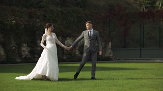 Lovely newlyweds caucasian bride groom walking in park, holding hands, wedding couple family