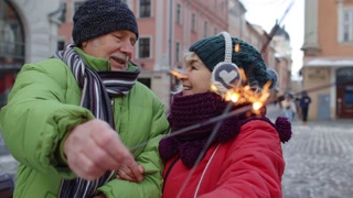 Senior couple kissing while strolling in winter city with burning sparklers in hand on street