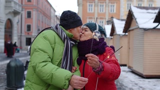 Senior couple kissing while walking through Christmas market with burning sparklers in hand on street